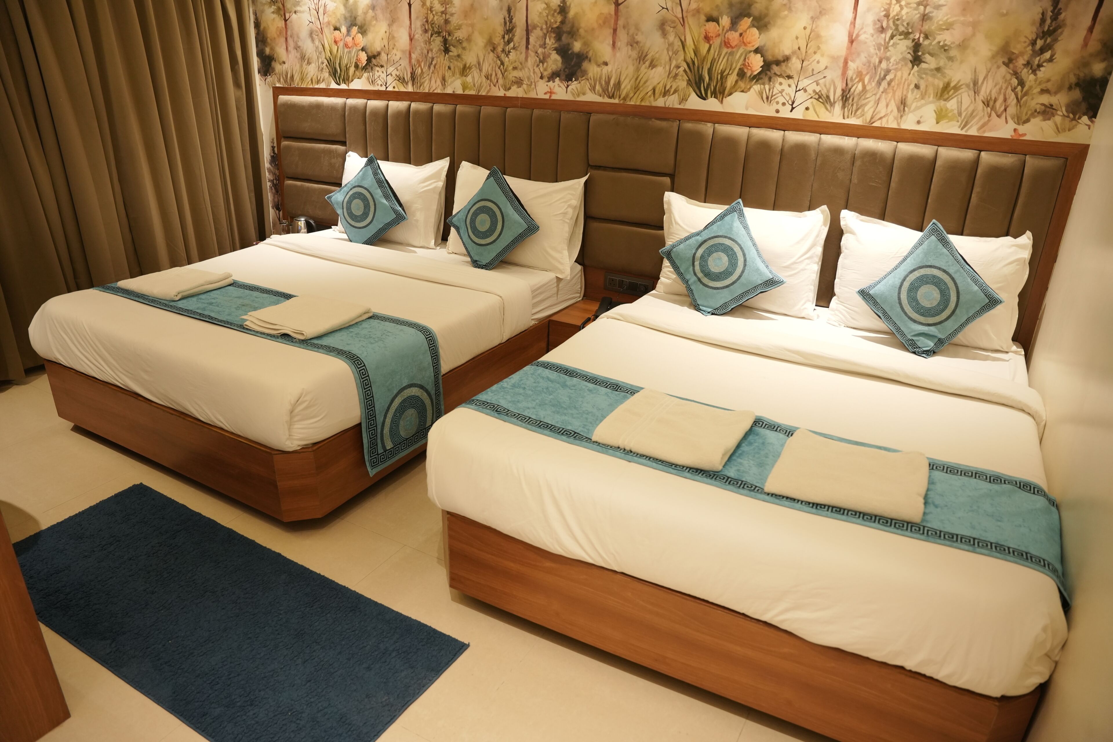 A hotel room with two beds, each with a headboard, blue and white bedding, and matching pillows.