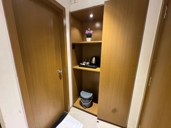A wooden closet with shelves containing a kettle, cups, and a flower vase. - Hotel Sai Seeta Palace Newly Renovated (Shirdi)