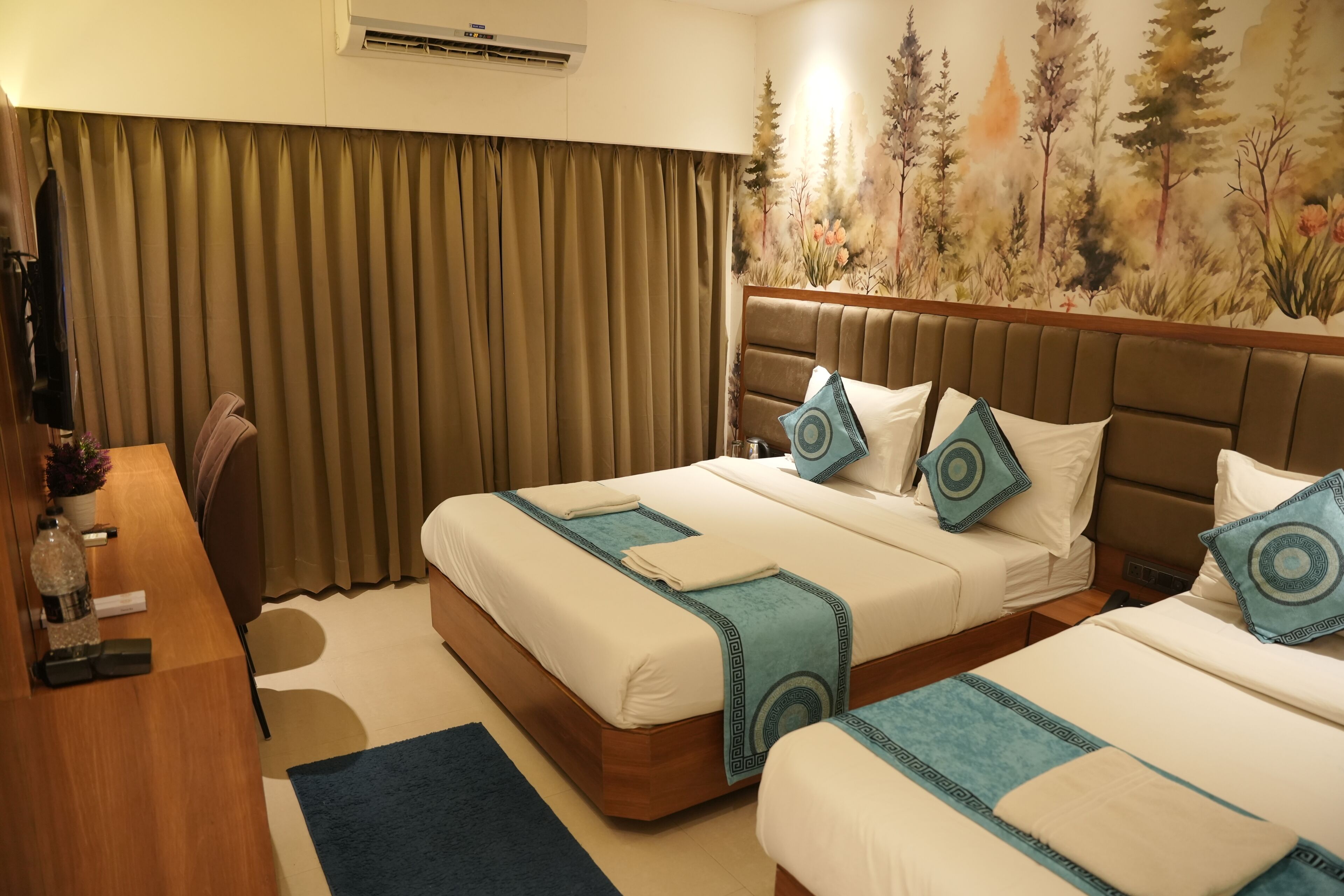 Habitación de hotel con dos camas, un escritorio, una silla, un ventanal con cortinas y un mural en la pared.