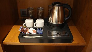 A coffee station with a kettle, two mugs, a tray with coffee packets, and a small electric heater.