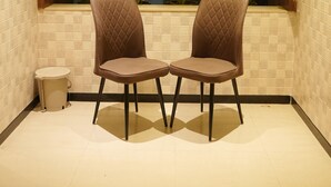 A corner with two chairs, a window with plants, and a tiled floor.
