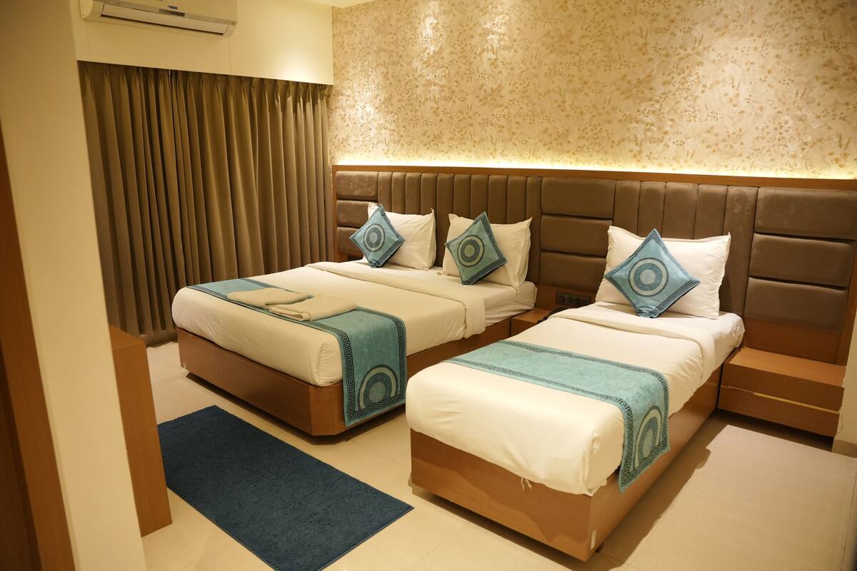 A hotel room with two beds, a headboard, a window with curtains, and a wall-mounted air conditioner.