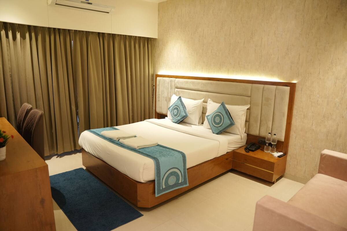 A hotel room with a bed, bedside table, nightstand, and a desk with a chair.