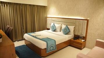 A hotel room with a bed, bedside table, nightstand, and a desk with a chair.