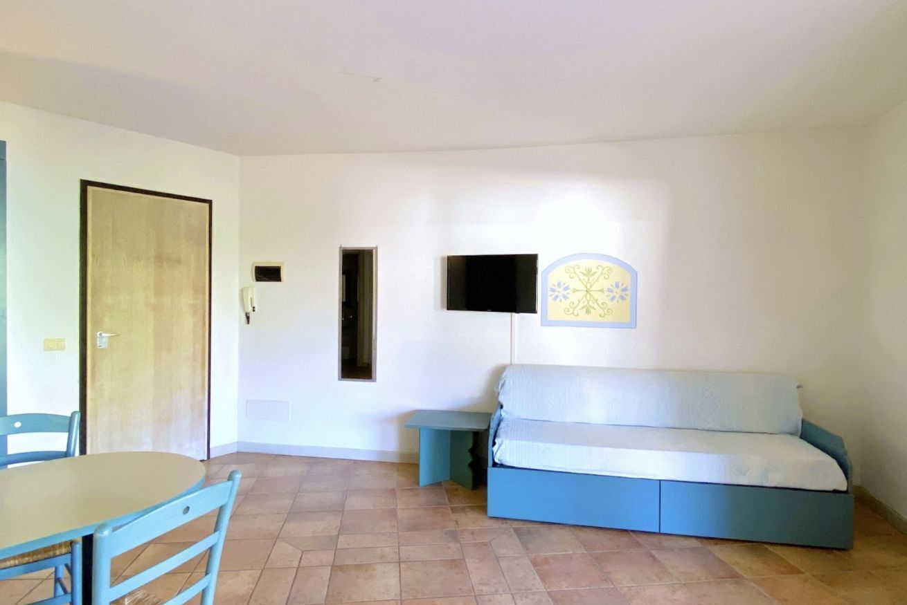 Une pièce avec un canapé bleu, une petite table, une chaise et un téléviseur fixé au mur.