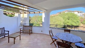 A covered outdoor area with a table and chairs, a pergola, and a view of greenery and buildings. - Charming two-room apartment of approximately 40 square meters with a 25 square meter covered veranda, located on the ground or first floor.It comprises a living room with a fully equipped kitchenette and a sofa bed, a bedroom with a double bed, and a bat (Porto Rotondo)