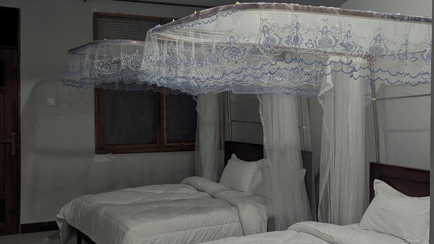 Un dormitorio con dos camas, un ventilador de techo y una ventana con cortinas.