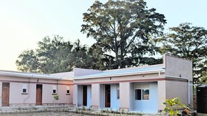 Un edificio de dos pisos con techo plano y un árbol grande al fondo.