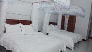 Habitación de hotel con dos camas individuales, cabecera de madera y dosel con cortinas traslúcidas.