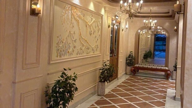 A spacious hallway with a tiled floor, a large wall mural, and a chandelier. - Ceylon Bake House Woodland Junction (Kanayannur)