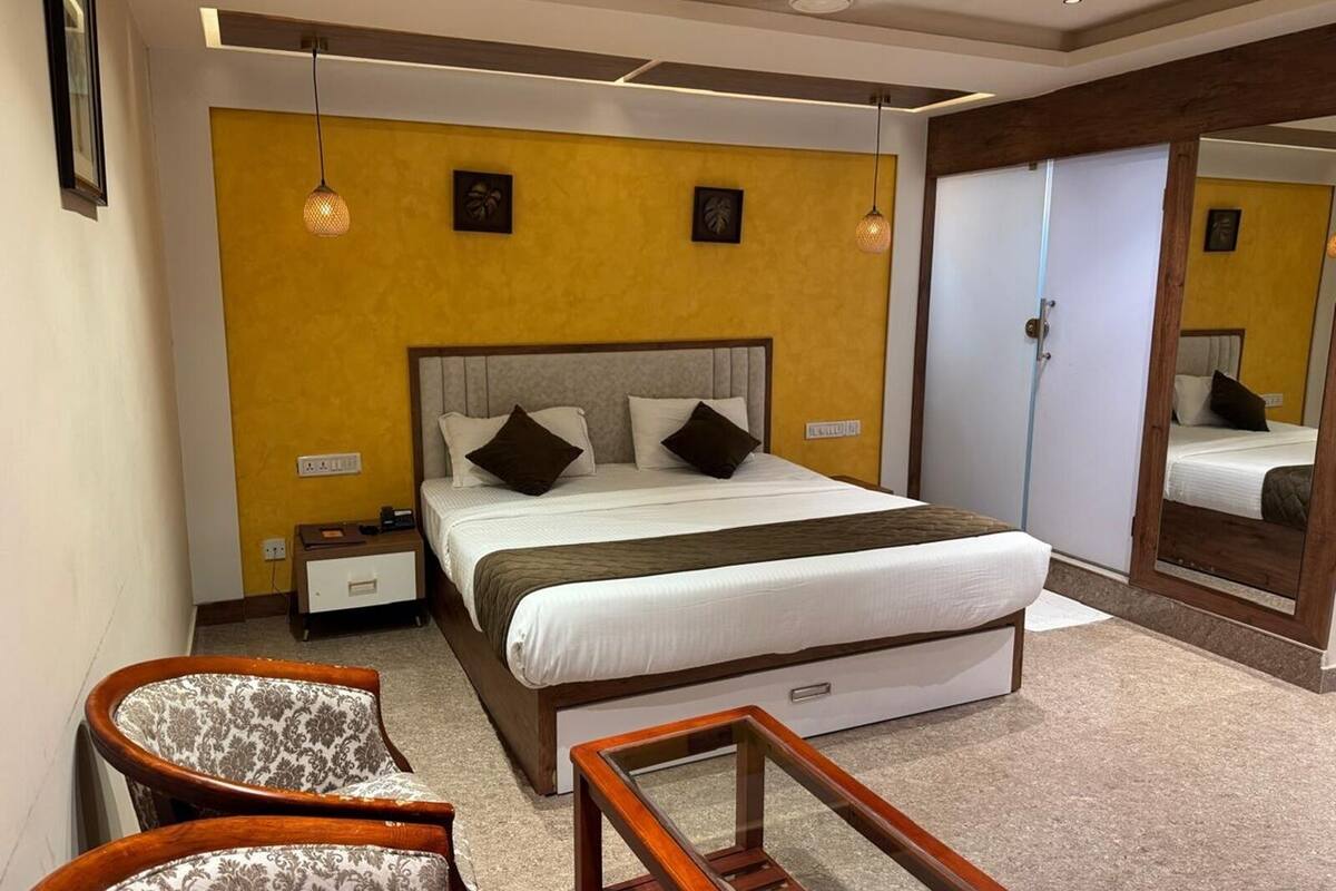 Una habitación de hotel con una cama grande, mesitas de noche, una silla, una pequeña mesa y un espejo.