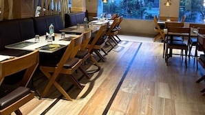 A restaurant with wooden furniture, a large window, and a view of greenery. - Ceylon Bake House Woodland Junction (Kanayannur)