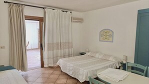 Una stanza con due letti, un tavolo, sedie, una finestra con tende, un condizionatore d'aria e un orologio a muro.