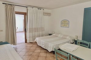 Habitación con dos camas, una mesa, sillas, una ventana con cortinas, un aire acondicionado y un reloj de pared.