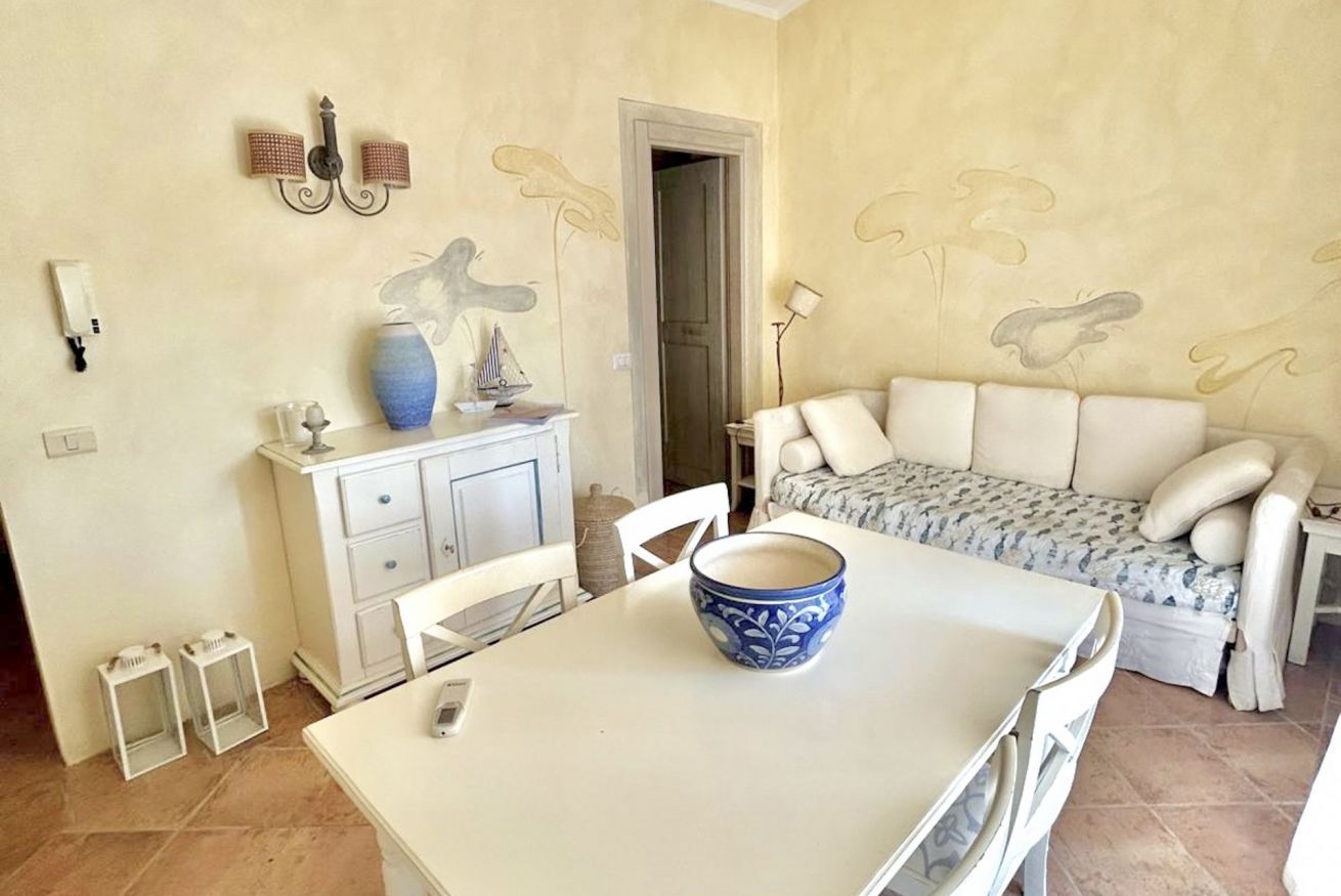 A room with a white table, a blue patterned bowl, a white sofa, and a cabinet with decorative items.