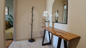 Un couloir avec une console en bois, un porte-manteau, une plante en pot et un miroir accroché au mur.