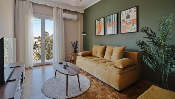 Un salon comprenant un canapé, une table basse, un téléviseur et une grande fenêtre avec des rideaux.
