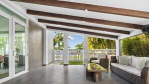Ein großzügiger Patio-Bereich mit Rattan-Sofa, Esstisch und Blick auf einen weißen Zaun und viel Grün.
