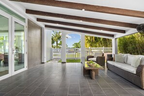 A spacious patio area with a wicker sofa, a dining table, and a view of a white fence and greenery. - Enchanted Hideaway with Private Pool (Puerto Rico)