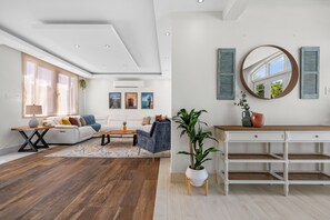 Ein geräumiges Wohnzimmer mit einem weißen Sofa, einem Couchtisch und Holzboden. Es gibt einen weißen Konsolentisch mit Schubladen und einen Spiegel darüber.