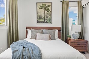 A neatly made bed with a patterned headboard, a bedside table with a lamp, and a framed botanical print on the wall. - Enchanted Hideaway with Private Pool (Puerto Rico)