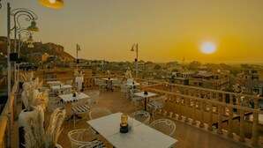 Een terras buiten met tafels en stoelen, met uitzicht op een stadsgezicht tijdens zonsondergang.