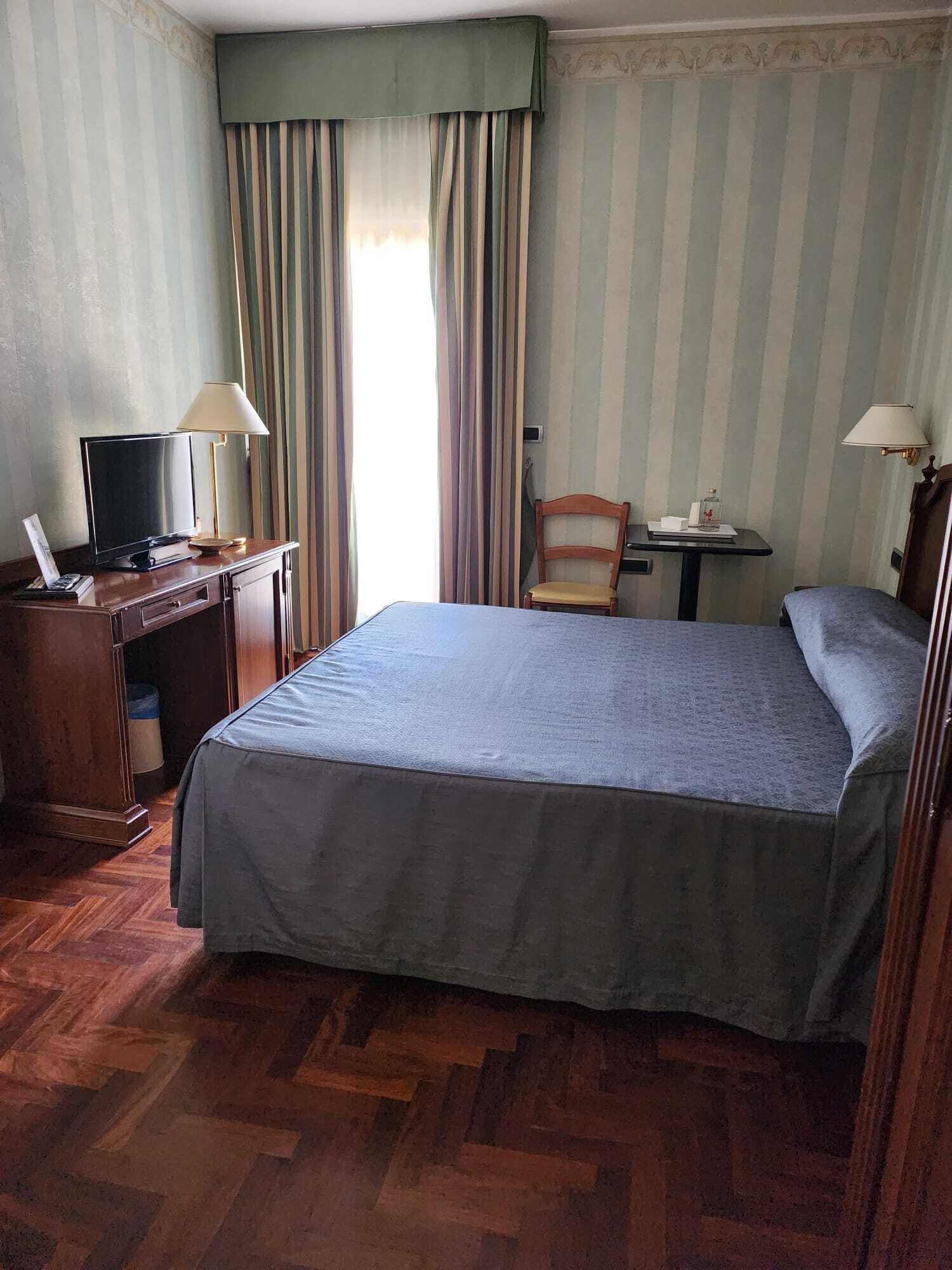 A hotel room with a bed, desk, chair, and a television.