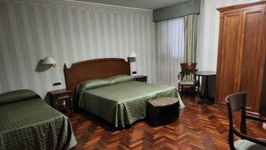A hotel room with two single beds, a wooden wardrobe, a small round table, and a chair.