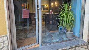 A hotel entrance with a glass door, a reception desk, and a potted plant.