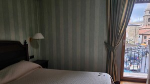A hotel room with a bed, a nightstand, a lamp, and a view of the street and a building through the window.