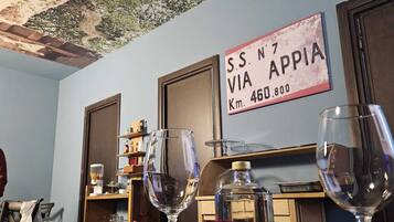 A dining area with a rustic ceiling, a sign indicating 'SS N7 VIA APPIA Km. 460,800', and a table with plates of food and wine glasses.