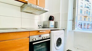 Eine kleine Küche mit Holdekor, einem Einbauofen, einer Waschmaschine und einem Fenster mit Blick auf die Stadt.