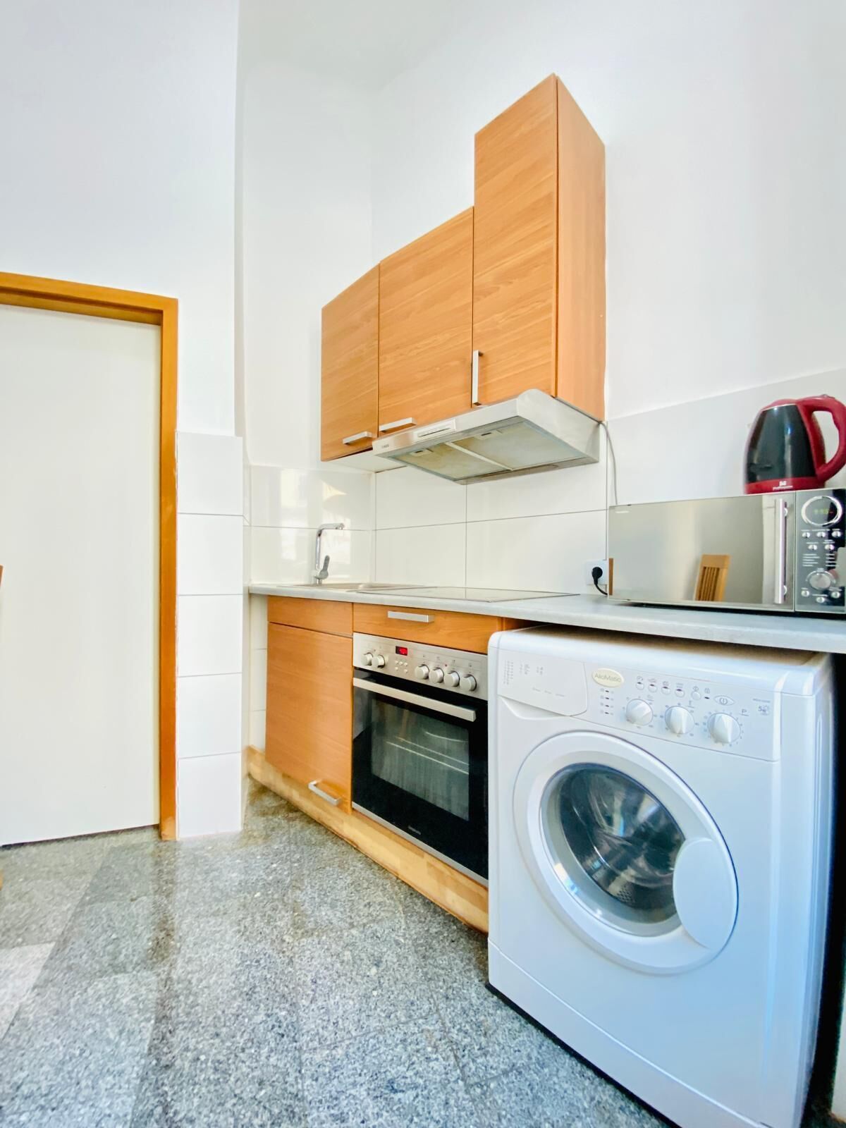 A compact kitchen with wooden cabinets, a built-in oven, a microwave, and a front-loading washing machine.