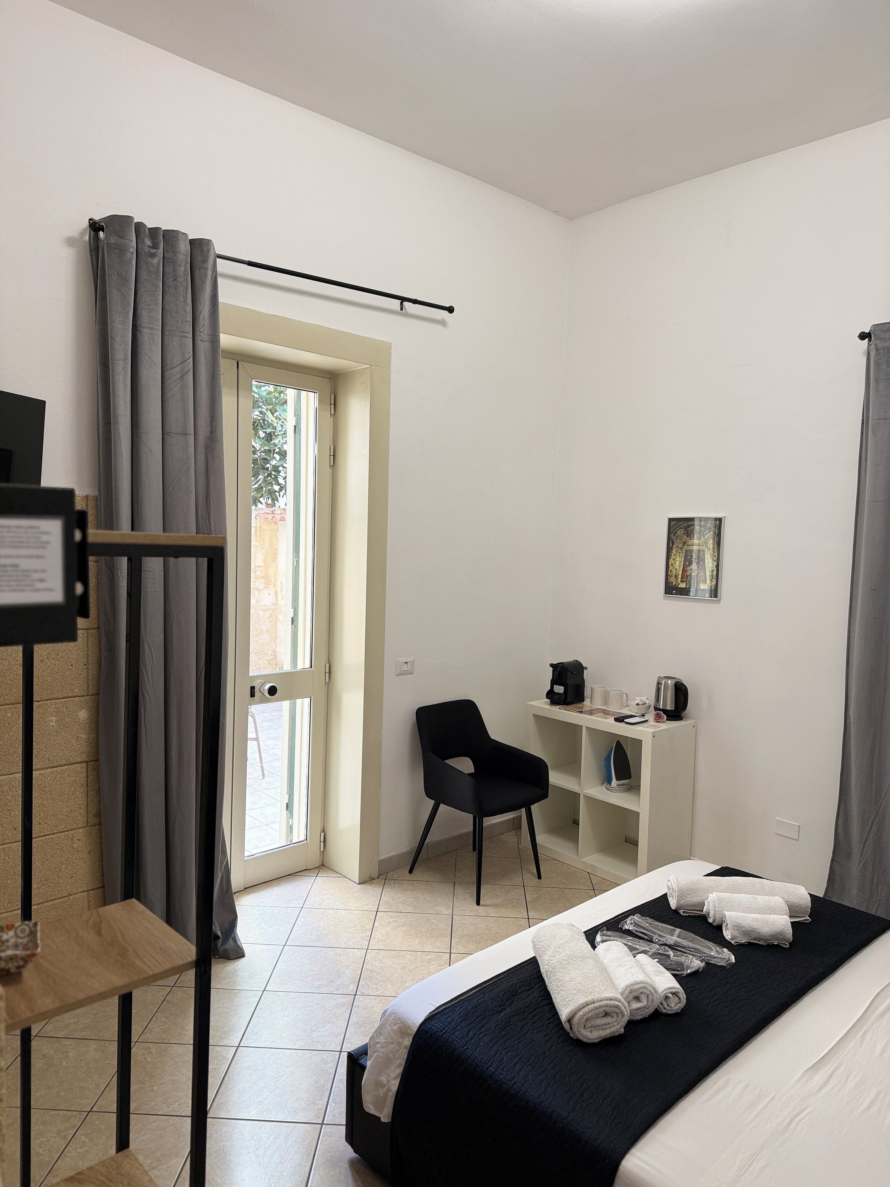Habitación de hotel con cama, escritorio con silla, una estantería pequeña y ventana con cortinas.