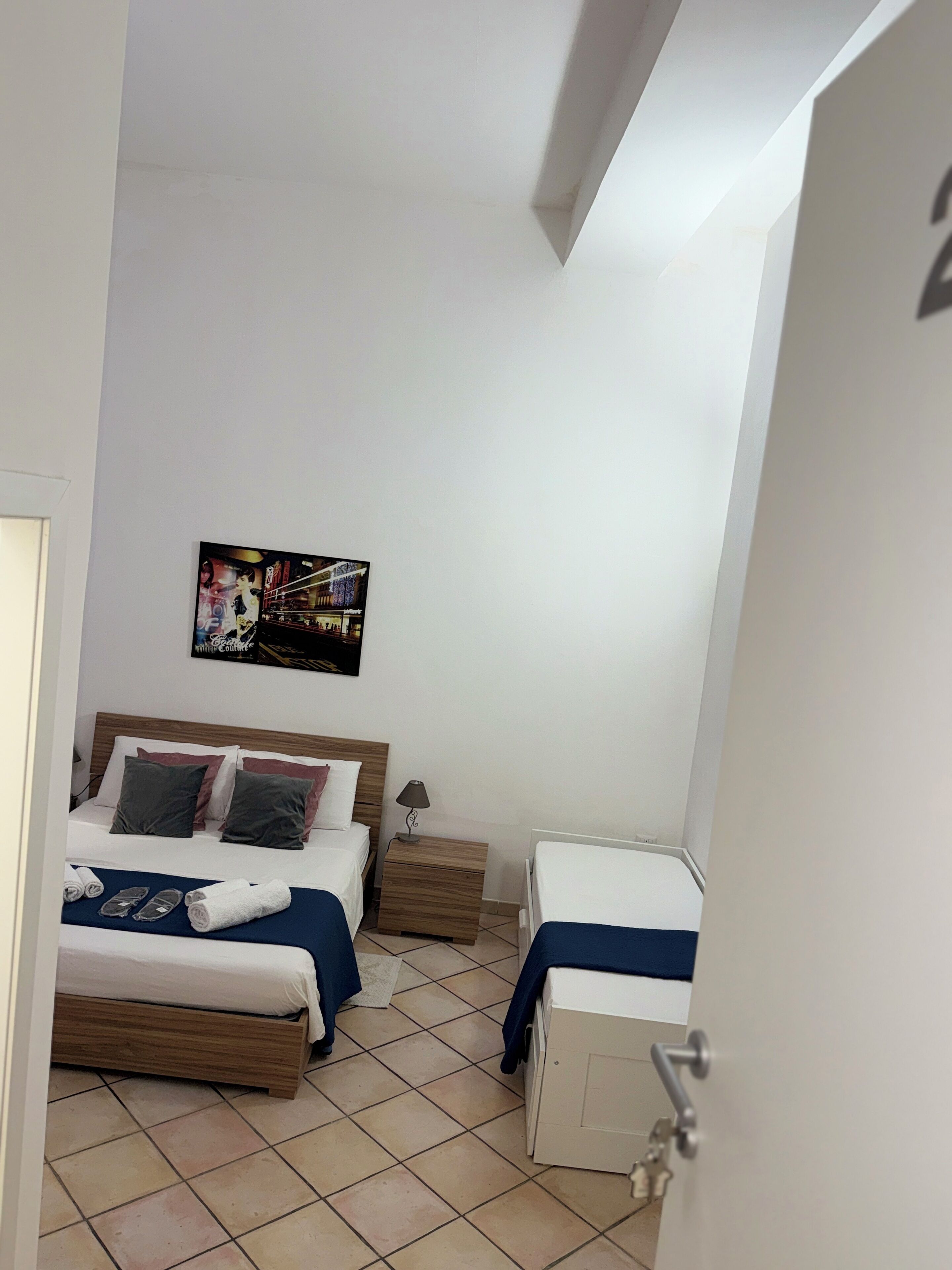 Ein Hotelzimmer mit zwei Betten, einem kleinen Nachttisch mit Lampe, einem Wandbild und einem weißen Kleiderschrank.