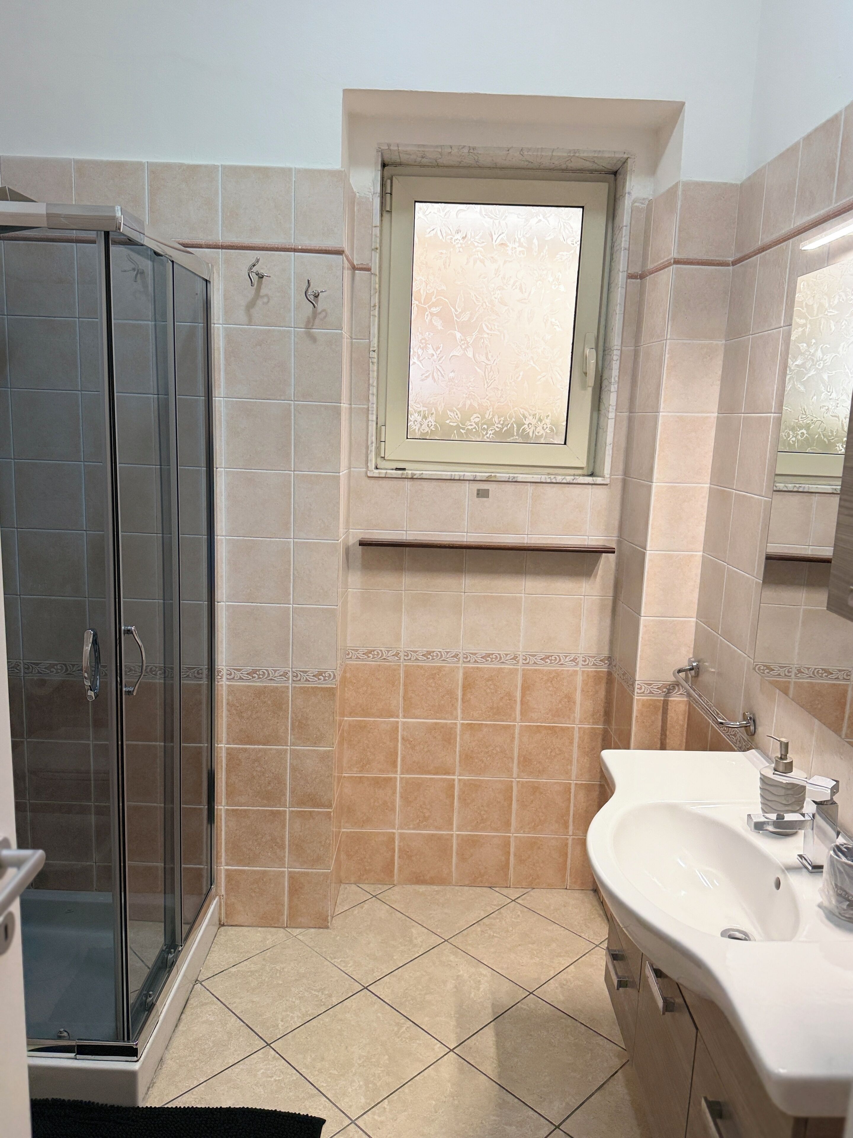 Une salle de bain avec une douche à parois de verre, un lavabo avec un miroir et une fenêtre au-dessus du lavabo.