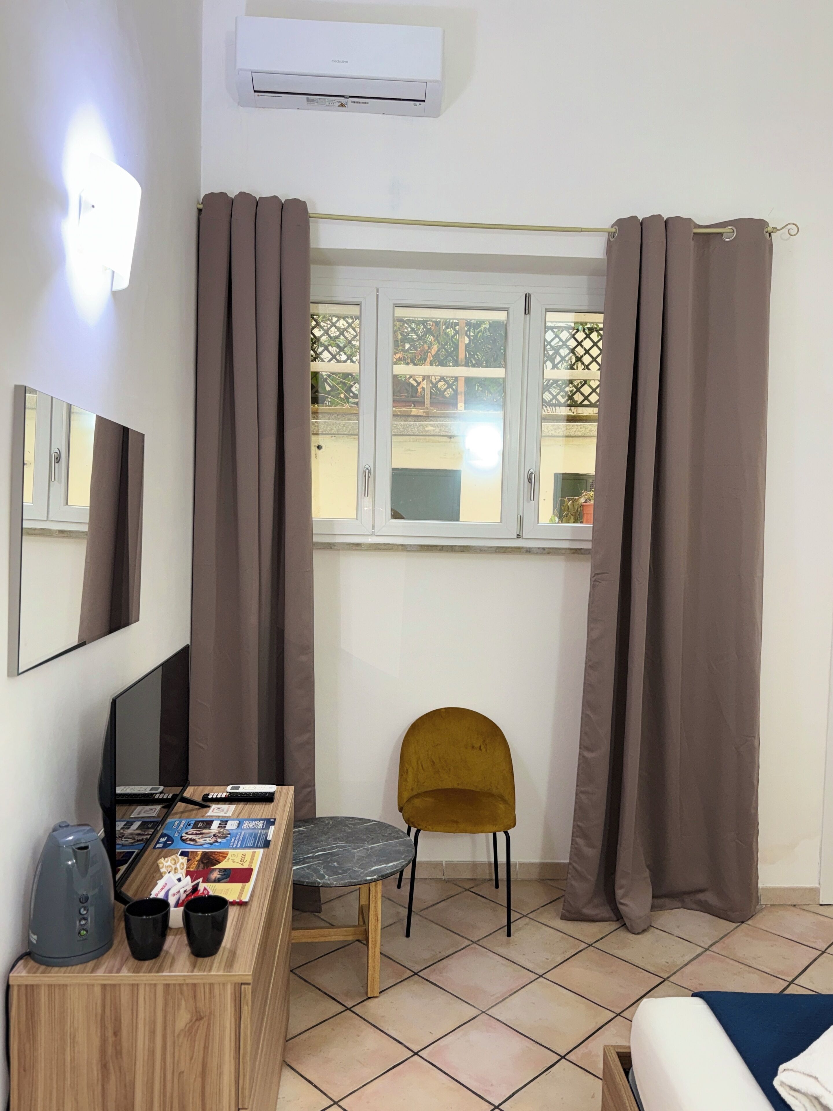 Quarto com cama, escrivaninha com laptop, cadeira e janela com cortinas.