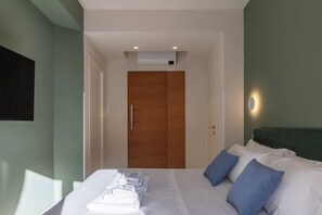 Hotellihuone, jossa on sänky, puinen vaatekaappi, seinälle asennettu ilmastointilaite ja yöpöytä, jossa on pyyhkeitä.