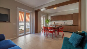 A modern living room with a blue sofa, a dining area with red chairs, and a kitchen with wooden cabinets. - ST PETER POSTCARD VIEW PENTHOUSE (Roma)