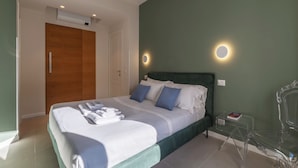 A modern bedroom with a large bed, a wooden wardrobe, a green accent wall, and a small bedside table with a book. - ST PETER POSTCARD VIEW PENTHOUSE (Roma)