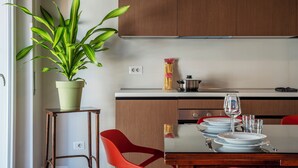 A modern kitchen with wooden cabinets, a dining table set with plates, glasses, and a red chair. - ST PETER POSTCARD VIEW PENTHOUSE (Roma)