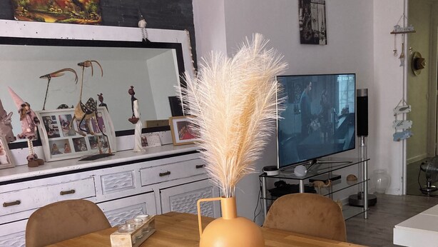 Una mesa de comedor con un florero de plumas de pampa, una vela y un mantel tejido.