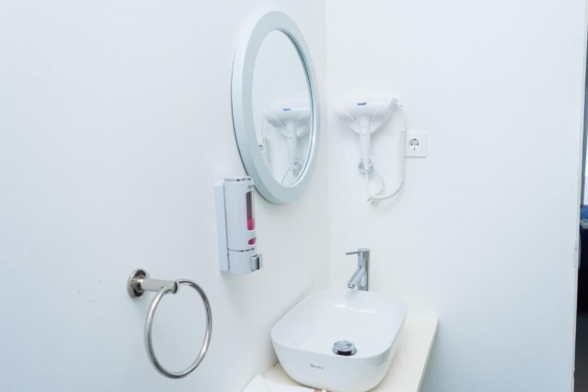 A bathroom with a white sink, a mirror, a towel ring, and a hand dryer.