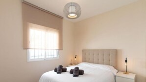 Ein Schlafzimmer mit einem großen Bett, einem Nachttisch, einer Lampe und einem Fenster mit Jalousien.