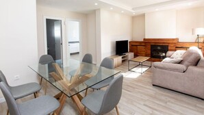 Ein modernes Wohnzimmer mit einem Glastisch, grauen Sesseln, einer Couch, einem Fernseher und einem Kamin.
