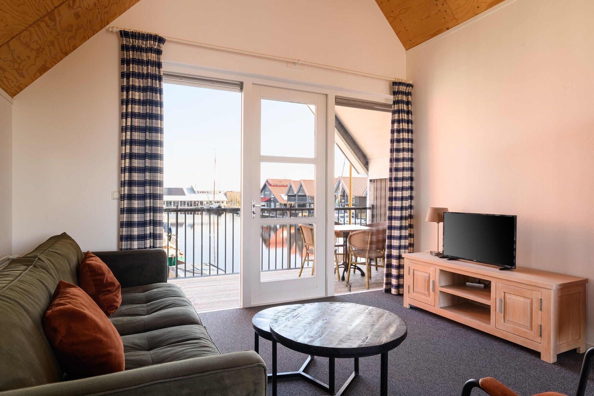 Een kamer met een bank, een tafel, een televisie op een houten kast en een schuifdeur naar een buitenbalkon.