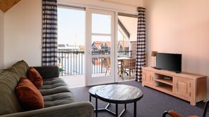 Et værelse med sofa, bord, fjernsyn på et træskab og en skydedør til en udendørs balkon.