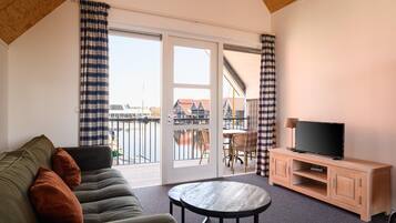 Een kamer met een bank, een tafel, een televisie op een houten kast en een schuifdeur naar een buitenbalkon.