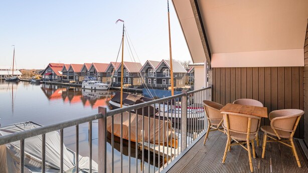 En balkon med fletmøbler med udsigt over en lystbådehavn med både og huse.