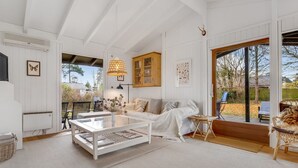 Een ruime woonkamer met een witte bank, een glazen salontafel en een groot raam met uitzicht op de omgeving.